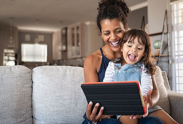 Young black mother and smiling daughter playing on digital tablet at home